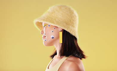 Image showing Beauty, makeup and woman with googly eyes in studio for weird, trendy and aesthetic on yellow background. Face, sticker and asian girl model with fun, weird and abstract expression while isolated