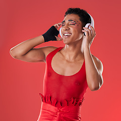 Image showing Dance, music and gay man with headphones isolated on a red background in a studio. Freedom, streaming and dancing lgbt person listening to a podcast, radio and audio on a backdrop for entertainment