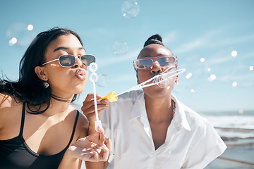 Image showing Friends, playing or blowing bubbles by beach, ocean or sea in summer holiday, travel vacation or bonding activity. Women, people or students and soap wand or toy in fun game, freedom or social break