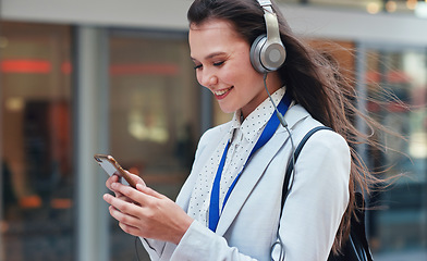 Image showing Business, woman in city and smartphone with headphones, smile or walking in town, streaming music or radio. Female professional, consultant or agent outdoor, cellphone or headset for podcast or urban