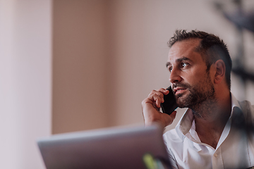 Image showing A businessman talking on his smartphone while seated in an office, showcasing his professional demeanor and active communication.