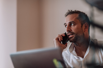 Image showing A businessman talking on his smartphone while seated in an office, showcasing his professional demeanor and active communication.