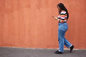 Image showing Black woman walking with smartphone in city, outdoor with technology, chat and communication with travel and fashion. Social media, urban street and wall with mockup and 5g, female in Jamaica