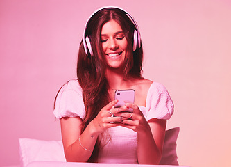Image showing Pink, light and music by woman in a bed with headphones, social media and streaming on wall background. Podcast, texting and girl relax in bedroom, happy and enjoying radio, audio or online playlist