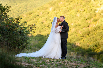 Image showing Full-length portrait of the newlyweds against the backdrop of brightly lit foliage, the newlyweds are kissing