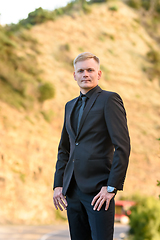 Image showing Portrait of a man in a formal black suit against the background of a mountain, in the rays of the setting sun