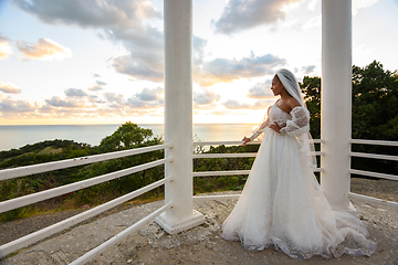 Image showing A bride in a wedding dress in a gazebo with columns on the seashore looks towards the sea