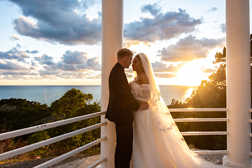 Image showing Portrait of newlyweds in a gazebo with columns in the rays of the setting sun