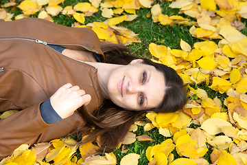 Image showing A beautiful girl of Slavic appearance joyfully lies on yellow autumn leaves in the park, close-up