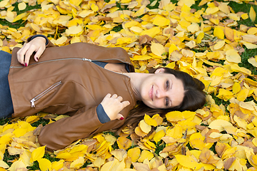 Image showing A beautiful girl of Slavic appearance joyfully lies on yellow autumn leaves in the park