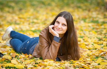 Image showing A beautiful girl of Slavic appearance in casual clothes lies on yellow autumn leaves