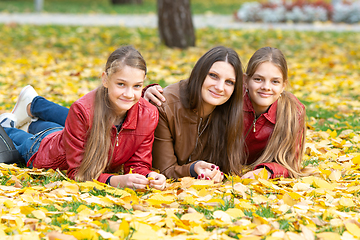 Image showing Mom and two daughters of a teenager of Slavic appearance in casual clothes lie on yellow autumn leaves