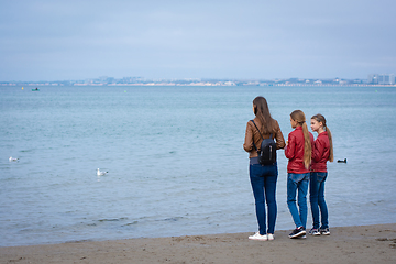 Image showing Mom and two daughters stand on the seashore on an autumn day, rear view
