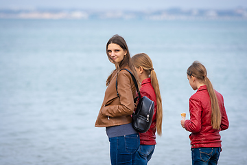 Image showing A mother and two daughters are standing on the seashore, the girl turned around and looked into the frame