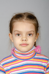 Image showing Close-up portrait of a disheveled five-year-old girl wearing a colored striped sweater on a gray background