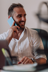 Image showing A businessman talking on his smartphone while seated in an office, showcasing his professional demeanor and active communication.