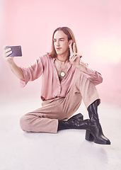 Image showing Selfie, peace and fashion with a gay man in studio on a pink background for lgbt inclusion or pride. Transgender, non binary and photograph with a male model sitting on the floor for trendy style