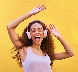 Image showing Music, freedom and dance with a black woman listening to the radio outdoor on a yellow wall background. Headphones, energy and face with an attractive young female streaming audio sound for fun