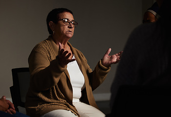 Image showing Counselling, mental health and a senior woman talking for therapy, meeting or psychology in a dark room. Patient, psychologist or therapist talking in group workshop, consultation or rehabilitation