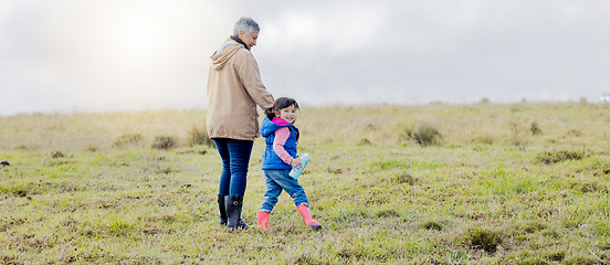 Image showing Grandmother, walking girl and nature park of a kid with senior woman in the countryside. Outdoor field, grass and elderly female with child on a family adventure on vacation with happiness and fun