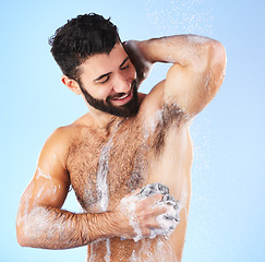 Image showing Shower, cleaning and man with sponge, soap and water splash in studio for wellness, hygiene and grooming. Skincare, health and happy male with foam, cosmetics and washing body on blue background