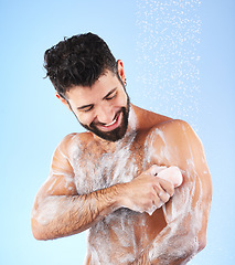 Image showing Soap, shower and man with water splash, smile and hygiene in studio for wellness, cleaning and grooming. Skincare, healthy skin and happy male with foam, cosmetics and washing body on blue background