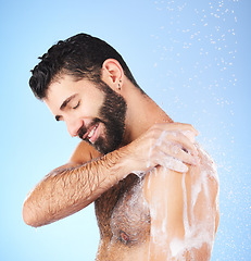 Image showing Shower, cleaning and man with water, smile and soap in studio for wellness, hygiene and grooming. Skincare, healthy skin and happy male with foam, bath cosmetics and washing body on blue background