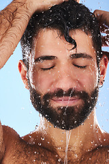 Image showing Washing, hair and man in studio for skincare, grooming and hygiene against blue background. Haircare, body care and guy model relax in shower, happy and isolated on water splash, cosmetic or wellness