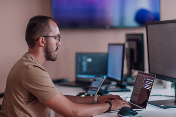 Image showing A programmer diligently testing smartphone applications while sitting in their office.