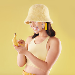 Image showing Woman, banana phone texting and studio with smile, communication and eyes sticker art on face. Asian model girl, yellow background and fashion with beauty, aesthetic and cosmetic wellness with fruit