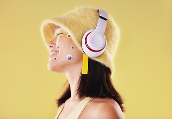 Image showing Makeup, music headphones and woman in studio isolated on a yellow background. Eye stickers, technology and smile of happy female model listening, enjoying and streaming radio, podcast and audio song.