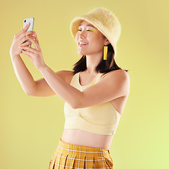 Image showing Selfie, beauty and smile of Asian woman in studio isolated on a yellow background. Makeup, fashion hat or young female model taking pictures or photo for social media, profile picture or happy memory