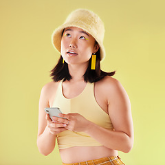 Image showing Phone, thinking and Asian woman typing in studio isolated on a yellow background. Ideas, technology or female model contemplating, decision or lost in thoughts with mobile for social media or texting