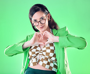 Image showing Portrait, hands and heart with a woman on a green background in studio for love, romance or health. Social media, emoji and affection with a trendy person posing or making a hand sign for style