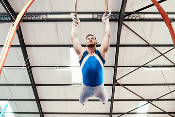 Image showing Man, acrobat and gymnastics swinging on rings in fitness for practice, training or workout at gym. Professional male gymnast hanging on ring circles for athletics, acrobatics or strength exercise