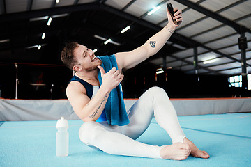 Image showing Man, gymnast and thumbs up for fitness selfie, profile picture or vlog in social media sitting on floor at the gym. Happy male acrobat smile for photo, memory or post showing thumb emoji, like or yes