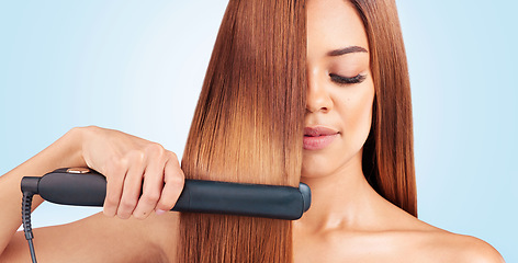 Image showing Face, beauty and woman with hair straightener in studio isolated on a blue background. Haircare, wellness and young female model with flat iron for salon treatment hairstyle, aesthetic or balayage.