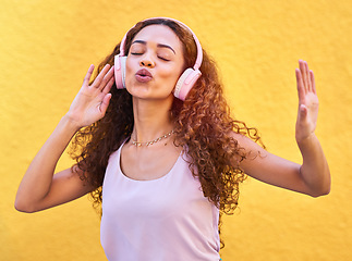 Image showing Music, freedom and singing with a black woman listening to the radio outdoor on a yellow wall background. Headphones, energy and face with an attractive young female streaming audio sound for fun