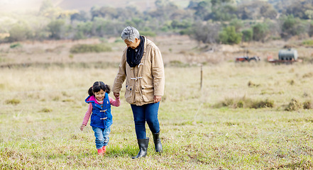 Image showing Grandma, girl and holding hands for walk on grass, family farm and bonding together with love outdoor. Old woman, child and helping hand in countryside, field and happiness in nature with landscape