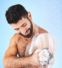 Image showing Body, shower and man with sponge, soap and water splash in studio for wellness, hygiene and grooming. Skincare, cleaning and happy male with foam, bathroom cosmetics and washing on blue background