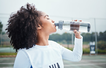 Image showing Sports, black woman and drinking water at court during training, workout and sport exercise outdoors. Fitness, thirsty and girl with bottle for wellness, hydration and recovery during practice