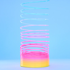 Image showing Rainbow slinky toy, spring and plastic product in studio isolated against a blue background mockup. Flexible toys, colorful spirals and childhood item stretched out for playing, having fun and games.