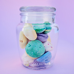 Image showing Glass jar, beach stones or rocks on table in studio isolated on a purple background. Beauty, art and variety of colorful pebbles in bottle collected from sea or ocean coast for interior decoration.