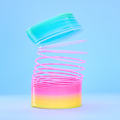 Image showing Rainbow slinky toy, spring and plastic product in studio isolated against a blue background mockup. Flexible toys, colorful spirals and childhood item stretched out for playing, having fun and games.