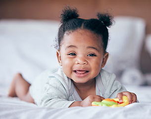 Image showing Happy, smile and portrait of a baby on a bed playing with a toy while relaxing in her nursery. Happiness, excited and girl infant or newborn laying in her bedroom while being playful in her house.