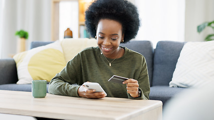 Image showing Young black woman shopping online using her phone and bank credit card in a bright living room. Banking and managing assets and finance using convenient wireless technology from the comfort of home