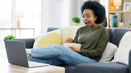 Image showing Happy african american woman streaming online movies on a laptop while snacking on popcorn and relaxing on a sofa at home. Black female enjoying a comedy, eating, laughing and having fun on a weekend
