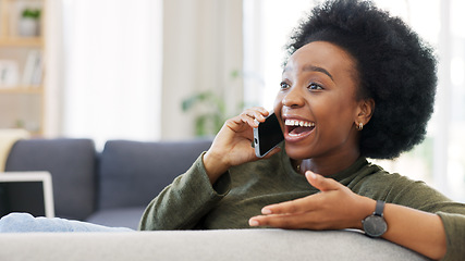 Image showing Happy African woman talking on the phone while relaxing on her cozy sofa at home. Cheerful black female with afro laughing while having a pleasant and funny conversation with a friend on her mobile