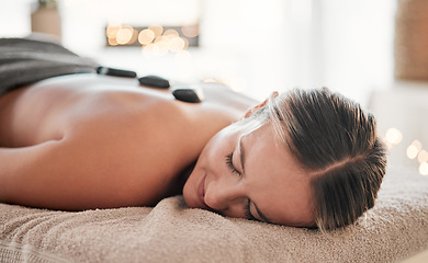 Image showing Woman, stone and back on bed in spa treatment for relaxation, stress relief or massage at resort. Happy female relaxing with hot rocks in physical therapy for body healing, zen wellness or skincare