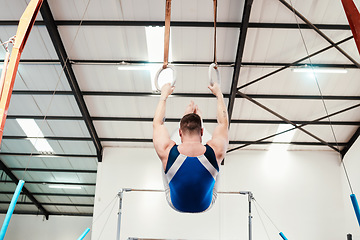 Image showing Man, acrobat and gymnast swinging on rings in fitness for practice, training or workout at gym. Professional male in gymnastics hanging on ring circles for athletics, acrobatics or strength exercise